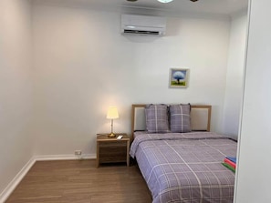 A bedroom with a bed, a nightstand with a lamp, and an air conditioning unit on the wall.