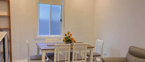 A dining area with a chandelier, a table with chairs, a sofa, and a window with blinds.
