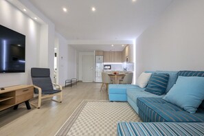 A modern living room with a sofa, a desk, and a TV. There is a kitchen area in the background. - SUNNY HILLS dream apartment (Finestrat)