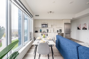 A modern kitchen with white cabinets, a blue sofa, and a dining table set for four. - High Rise 1BR Condo w Balcony Beautiful Views (Kitchener)