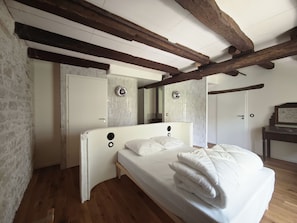 Une chambre avec un lit blanc, des poutres en bois, une porte blanche et un mur recouvert de carreaux.