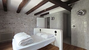 A bedroom with a wooden floor, a white bed, a stone wall, and a white ceiling. - Domaine du Moulin Français - Along the River (Champougny)