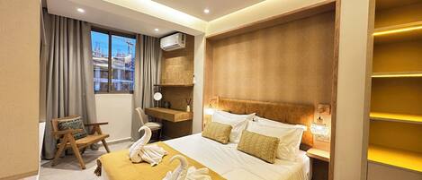 A hotel room with a large bed, a desk, a chair, and a view of the cityscape through the window.