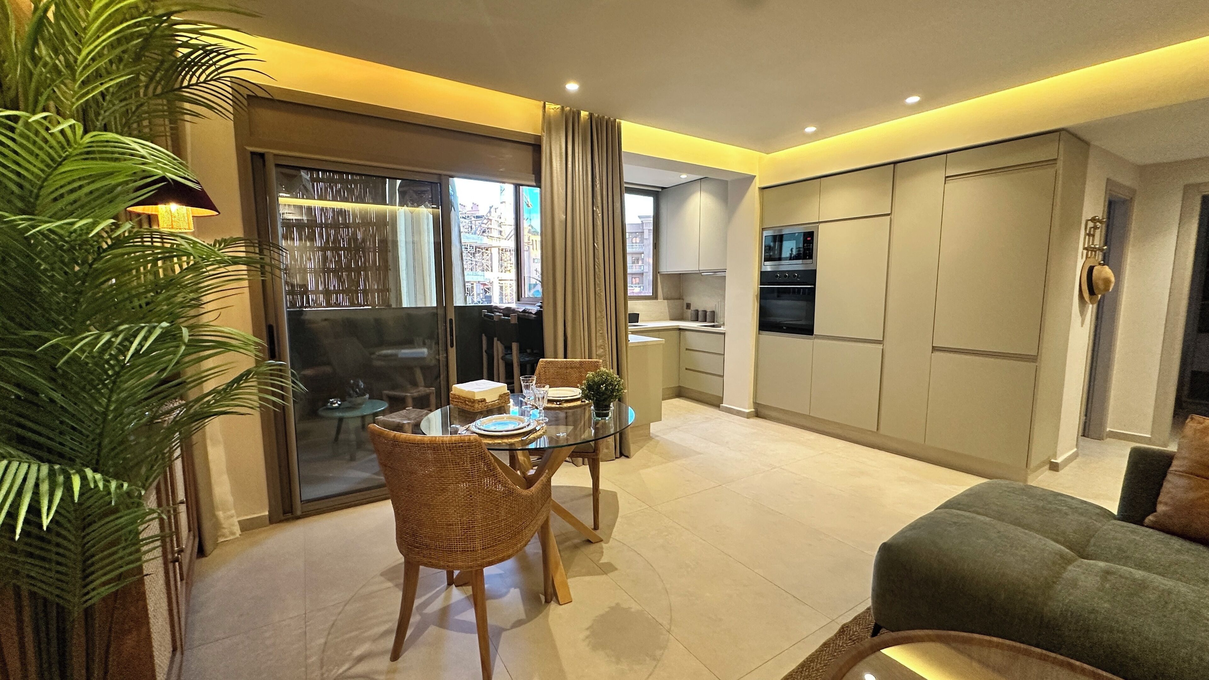 A modern living area with a dining table, chairs, a sofa, and a kitchen with cabinets and appliances.