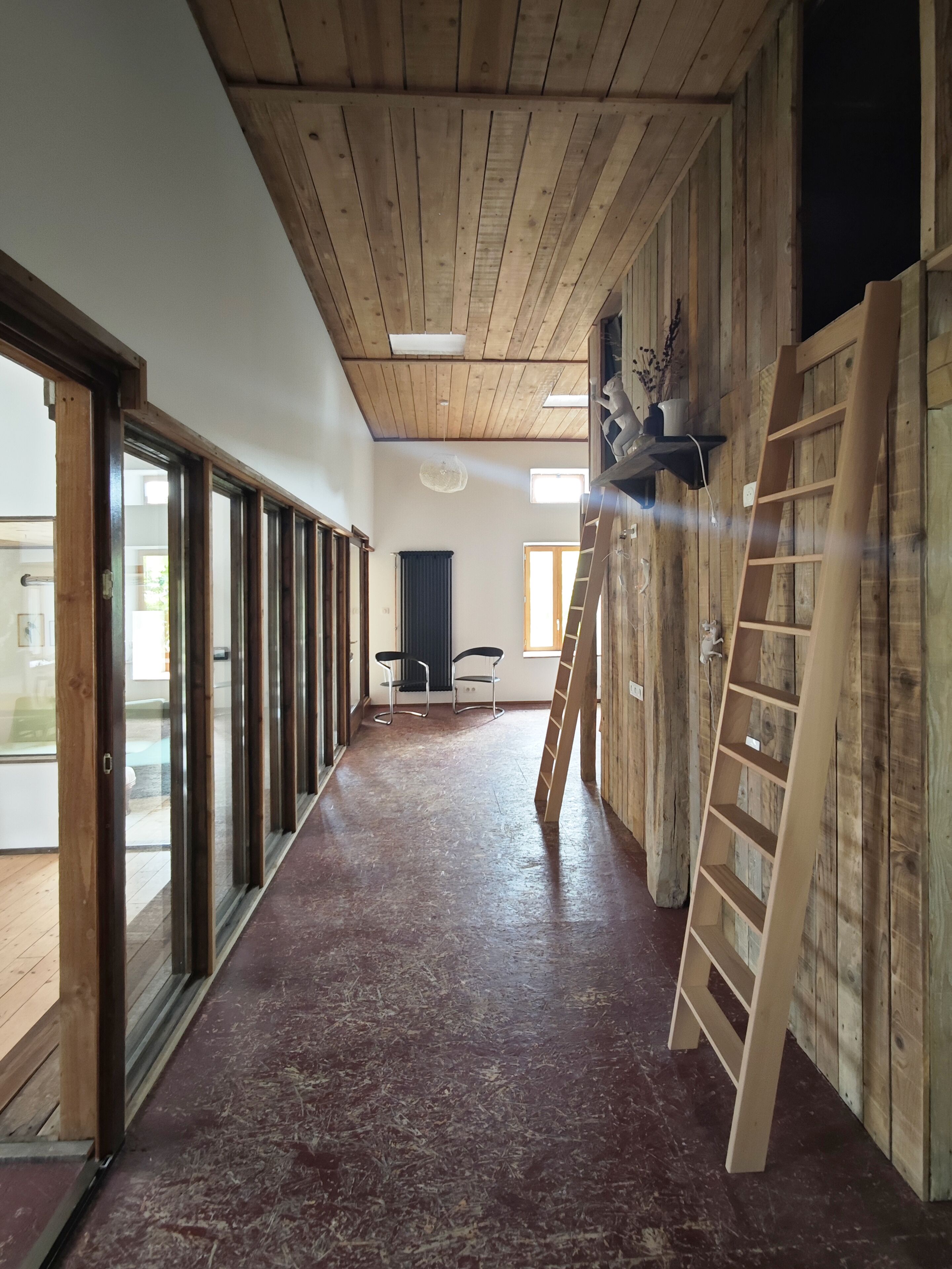 Ein Flur mit Holzboden, Deckenbalken aus Holz und Blick ins Freie durch Glasüren.