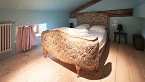 A bedroom with a floral-patterned bed, wooden beams, a radiator, and a window with curtains. - Domaine du Moulin Français - Outdoors (Champougny)
