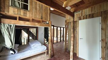 Une pièce rustique en bois, avec un lit superposé, une porte blanche et une fenêtre avec des rideaux.