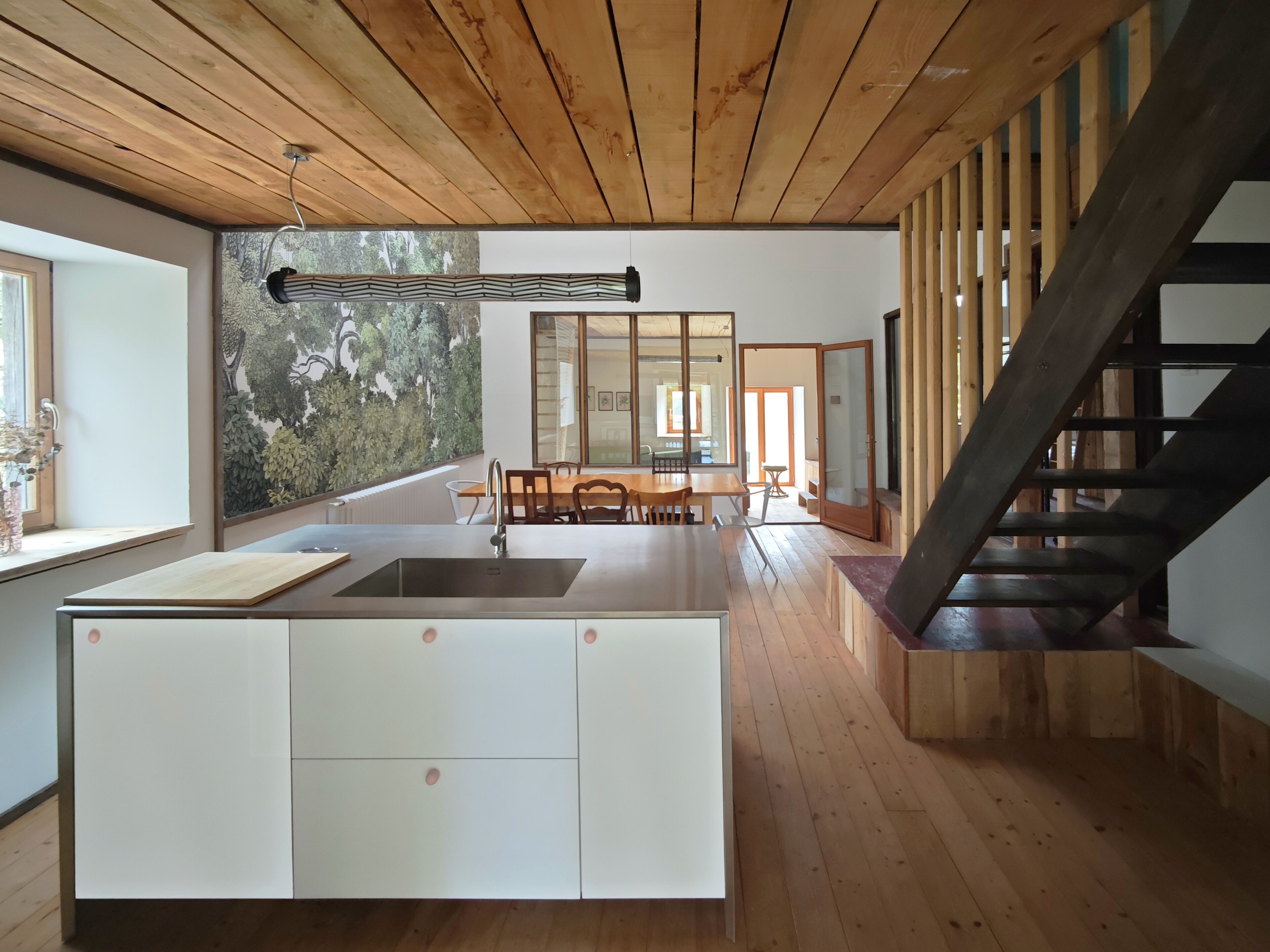 Une cuisine moderne dotée d’un îlot central, de planchers en bois et d’un escalier menant à un niveau supérieur.