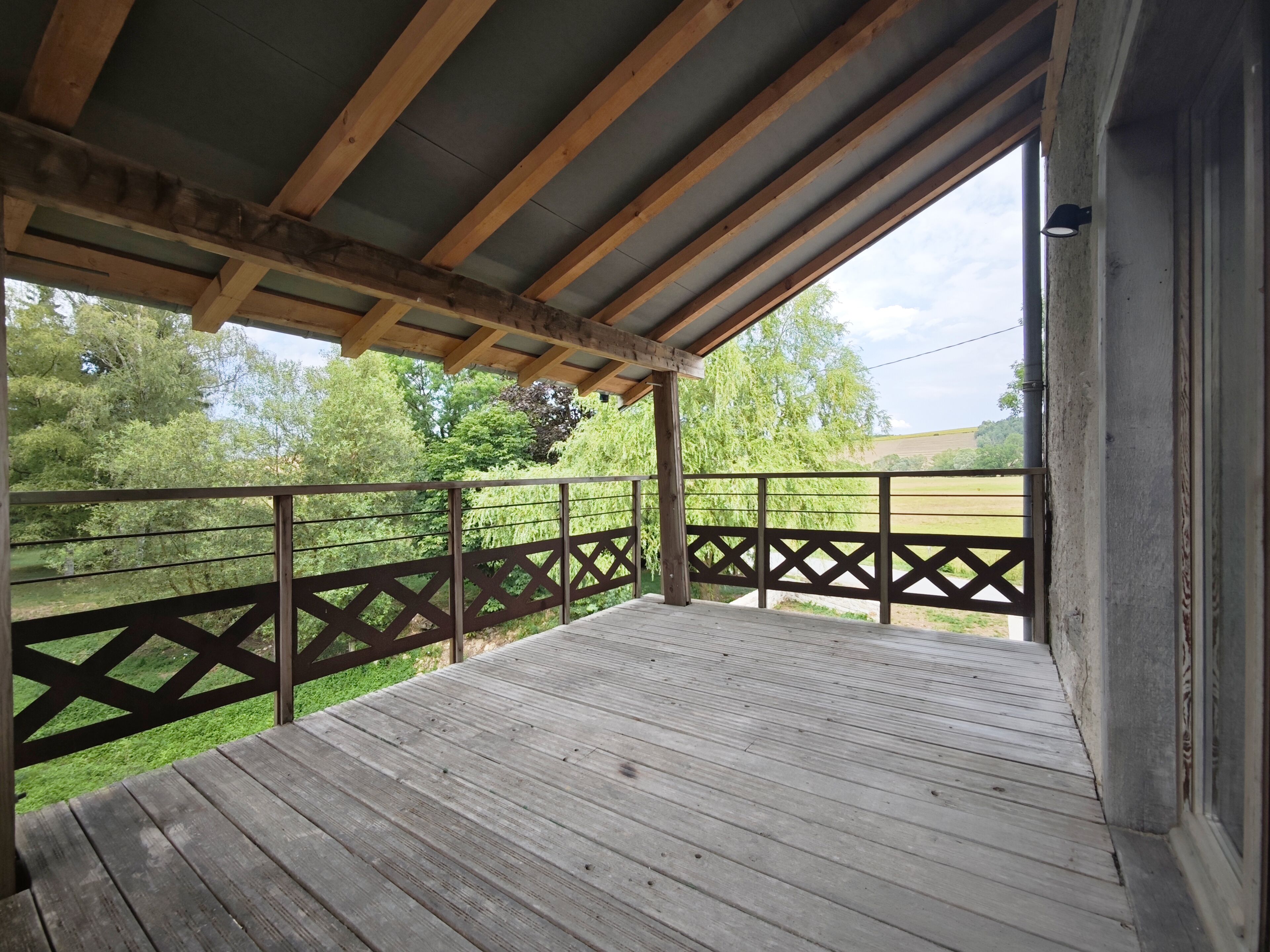 A wooden deck with a metal railing, overlooking a grassy area and trees.