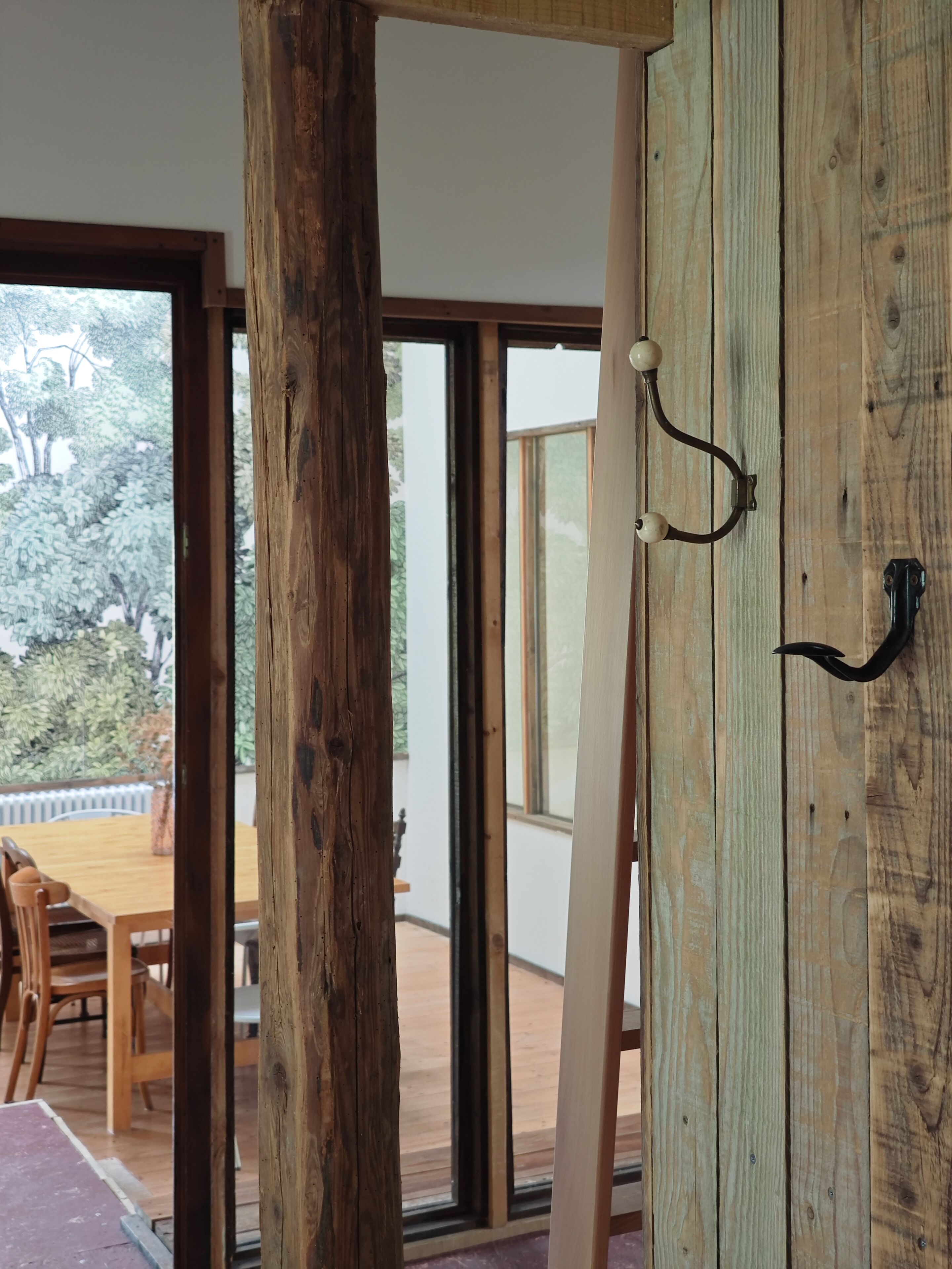 A room with a wooden door, a dining area with a table and chairs, and a view of the outdoors through large windows.