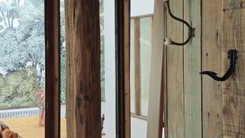 A room with a wooden door, a dining area with a table and chairs, and a view of the outdoors through large windows.