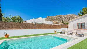 Una piscina amb superfície d'aigua transparent i blava, envoltada per una paret blanca i una zona verda. Hi ha gandules i una planta en test propera a la piscina.