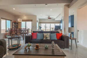 Ein geräumiges Wohnzimmer mit einem dunkelgrauen Sofa, einem Couchtisch mit Dekoration und einem Essbereich mit einem Glaskabinett.
