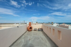Eine Dachterrasse mit einem Terrakotta-Topf, einem Magazin-Ständer und Blick auf das Meer und Gebäude.