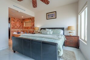 Ein modernes Schlafzimmer mit einem großen Bett, Nachttischen, einem Fenster und einem im Hintergrund sichtbaren Badezimmer.