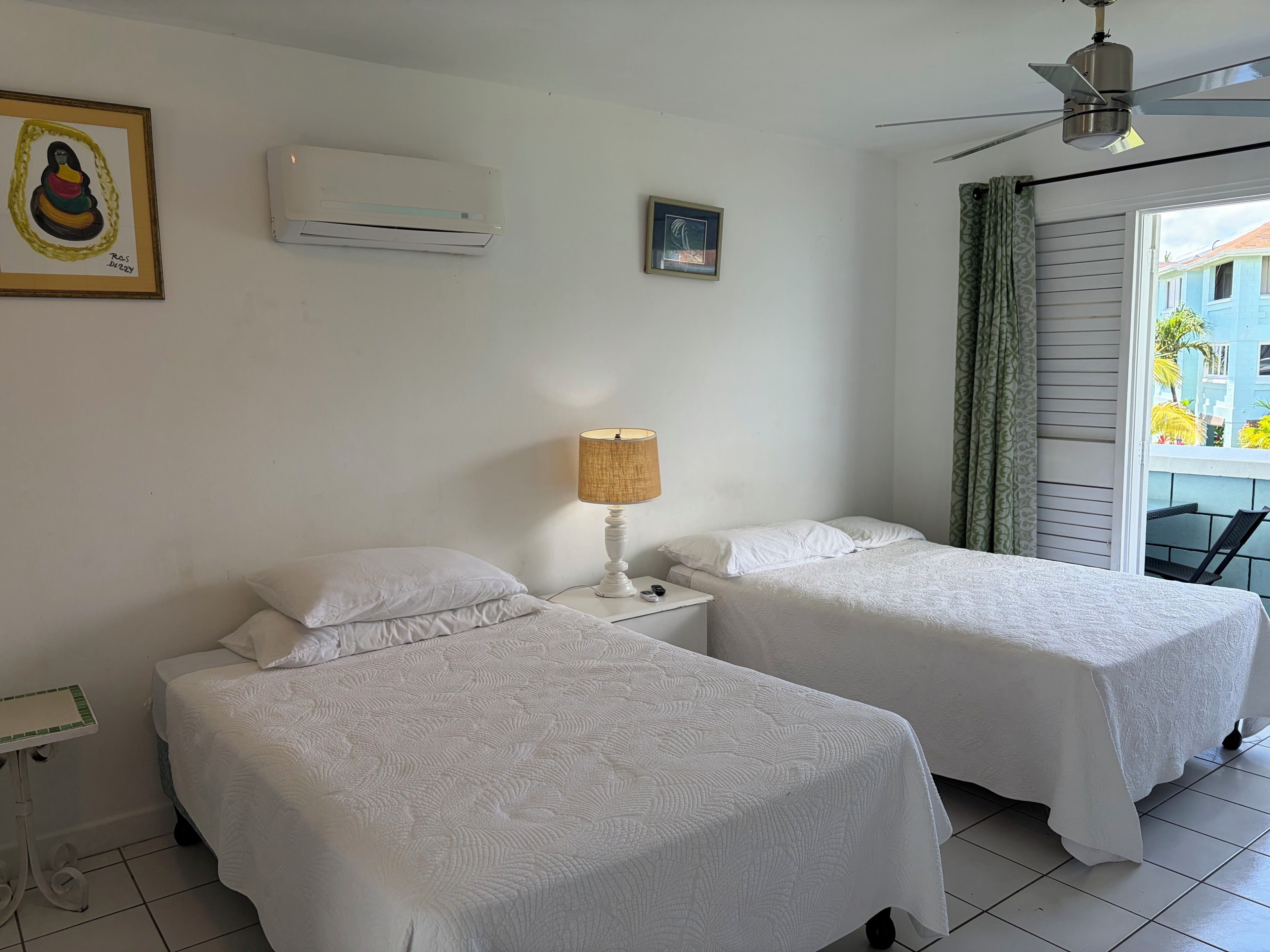 Une chambre d’hôtel avec deux lits, une table de chevet avec une lampe, un climatiseur et un ventilateur de plafond.