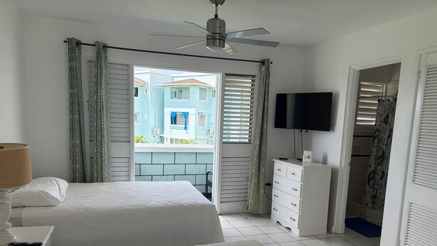 Habitación de hotel con dos camas, ventilador de techo, televisión y vistas a edificios exteriores.