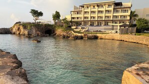 Un hotel frente al mar con piscina, un puente y un litoral rocoso.