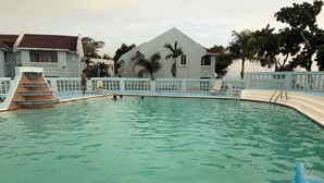 Una piscina con un cartel de prohibido bucear, un tobogán de agua azul y una escalera de acceso a la piscina.