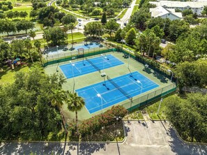 Vista aérea de un complejo de canchas de tenis con varias canchas, rodeado de árboles y un estacionamiento.