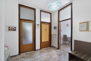 Un pasillo con piso de mármol, puertas de madera, un candelabro en el techo y un reloj en la pared.