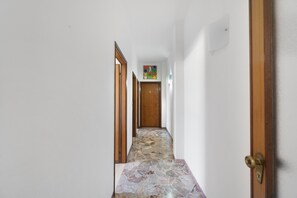 A hallway with a stone-tiled floor, wooden doors, and a colorful artwork on the wall. - Aaron Guest House - 4-Bedroom Apartment in Marghera (Venice)