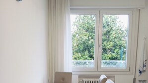 Ein Essbereich mit einem Tisch für vier Personen, einer Uhr an der Wand und einem Fenster mit Blick auf Grünflächen.