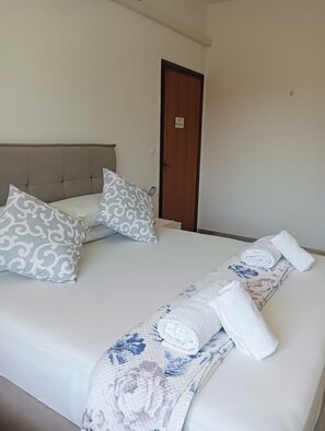 Een hotelkamer met een bed, kussens, een deur en handdoeken.