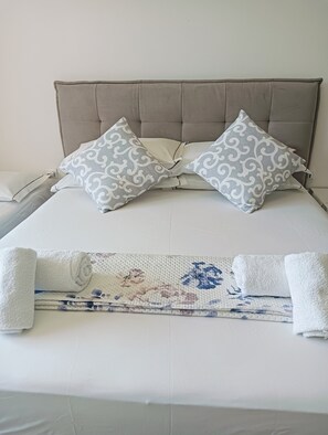 A neatly made bed with a patterned bedspread, two pillows with a swirled design, and two rolled towels. - Aaron Guest House - 4-Bedroom Apartment in Marghera (Venice)