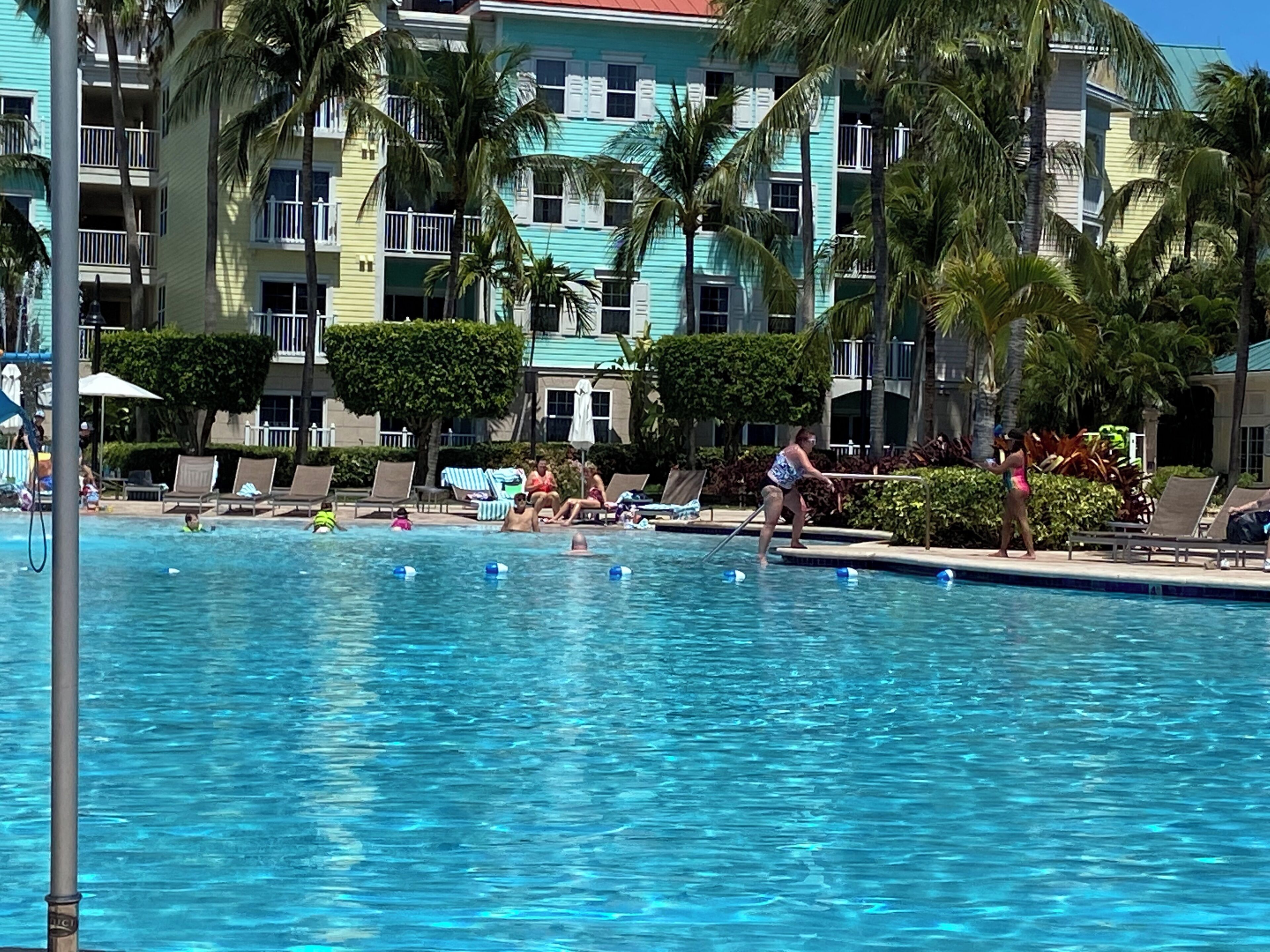 Piscina com espreguiçadeiras e palmeiras, cercada por edifícios altos com varandas.
