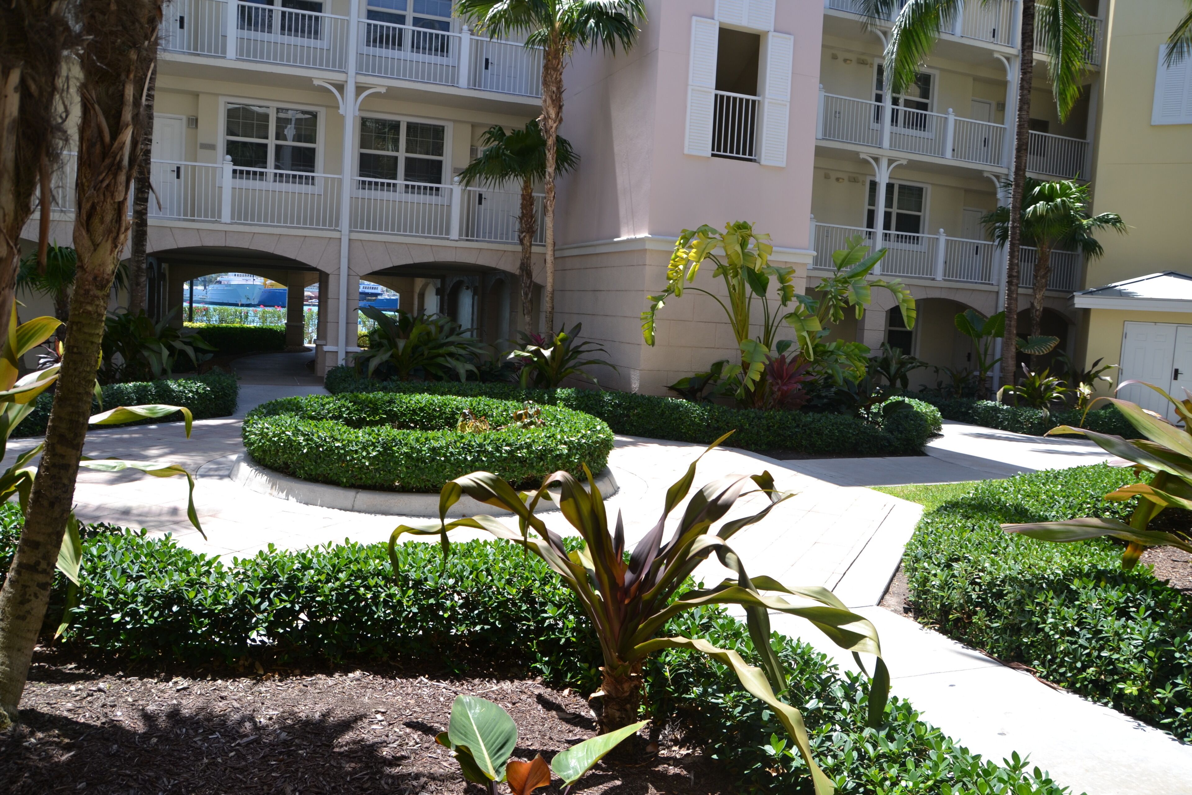 A hotel courtyard with a central circular garden, palm trees, and a multi-story building with balconies.