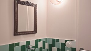 Un bagno con parete rivestita in piastrelle verdi e bianche, un piano d'appoggio in legno, un lavandino, uno specchio e una porta.