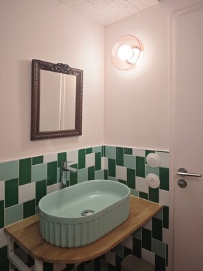 Un baño con pared de azulejos verdes y blancos, encimera de madera, lavamanos, espejo y puerta.
