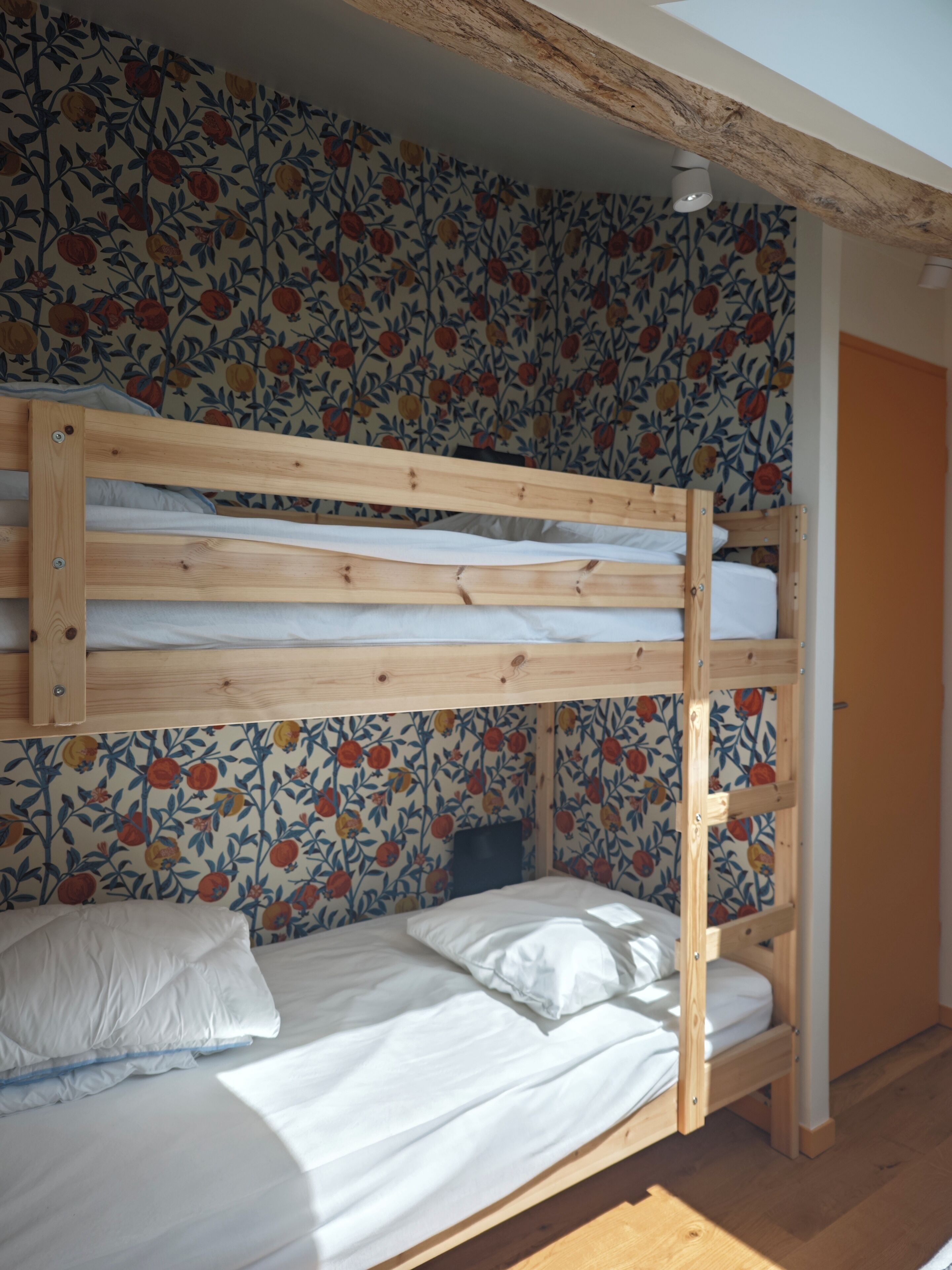 Een stapelbed met houten frame, witte beddengoed en behang met een bloemenprint.