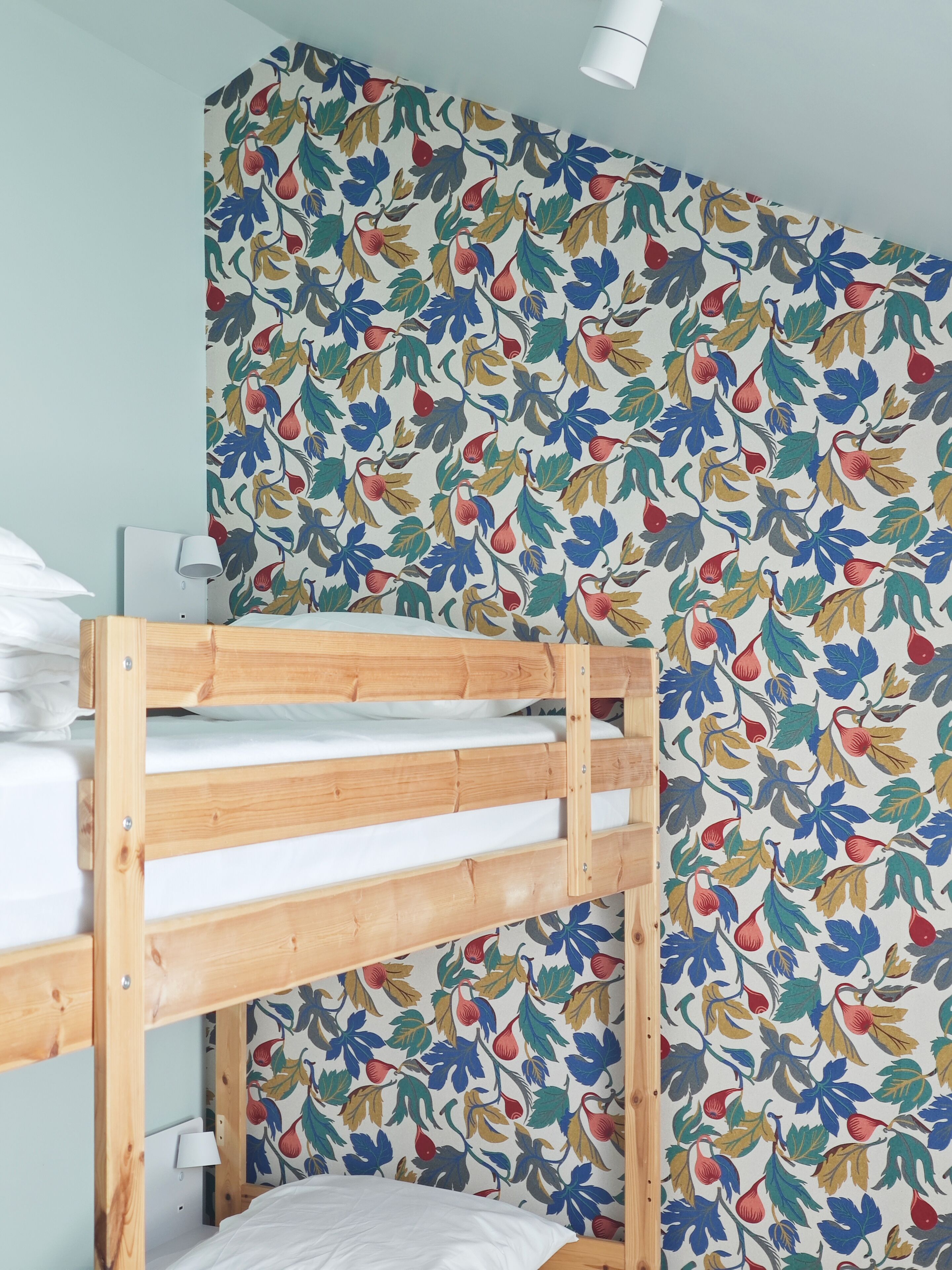 A bunk bed with a wooden frame and white bedding, a white lamp, and a wall with a floral pattern.
