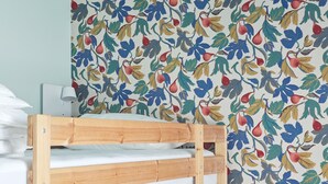 Un letto a castello con struttura in legno e biancheria bianca, una lampada bianca e una parete con motivo floreale.