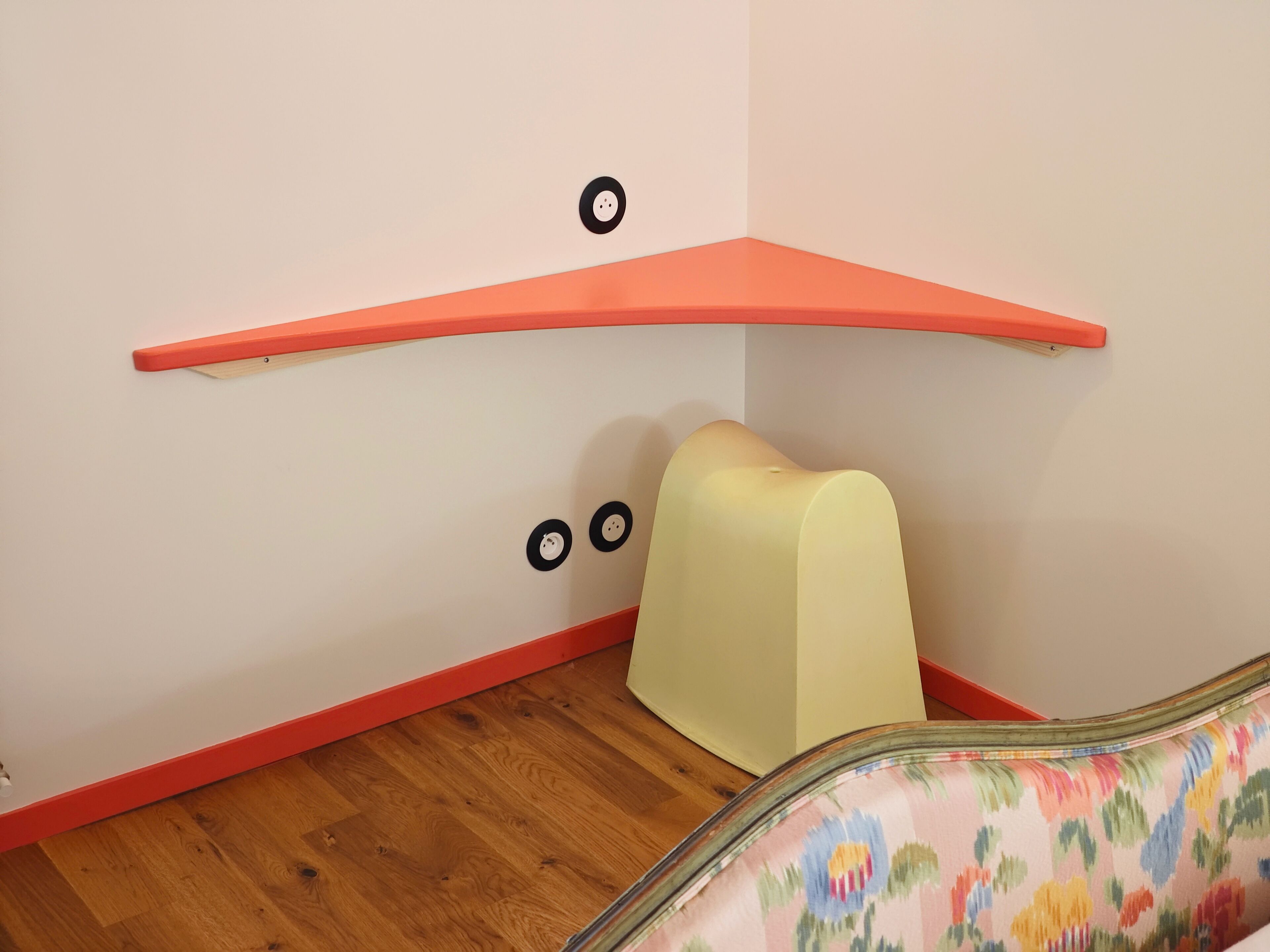 Un coin de pièce avec un plancher en bois, un mur blanc et une plinthe rouge.