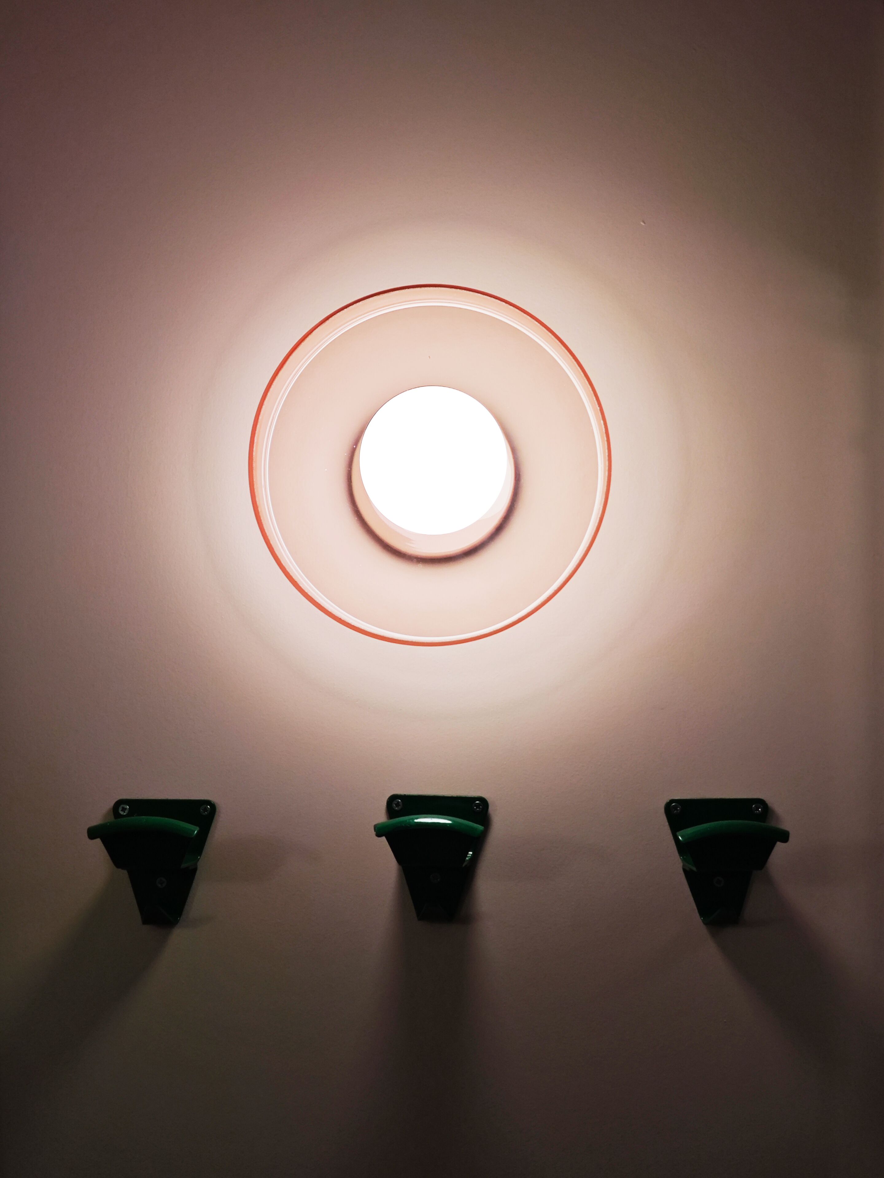 Un luminaire mural de forme circulaire, doté de trois interrupteurs verts situés en dessous.
