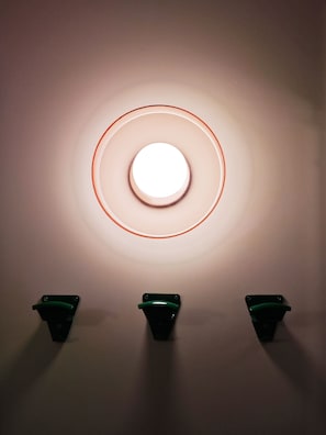A wall-mounted light fixture with a circular design and three green switches below it.
