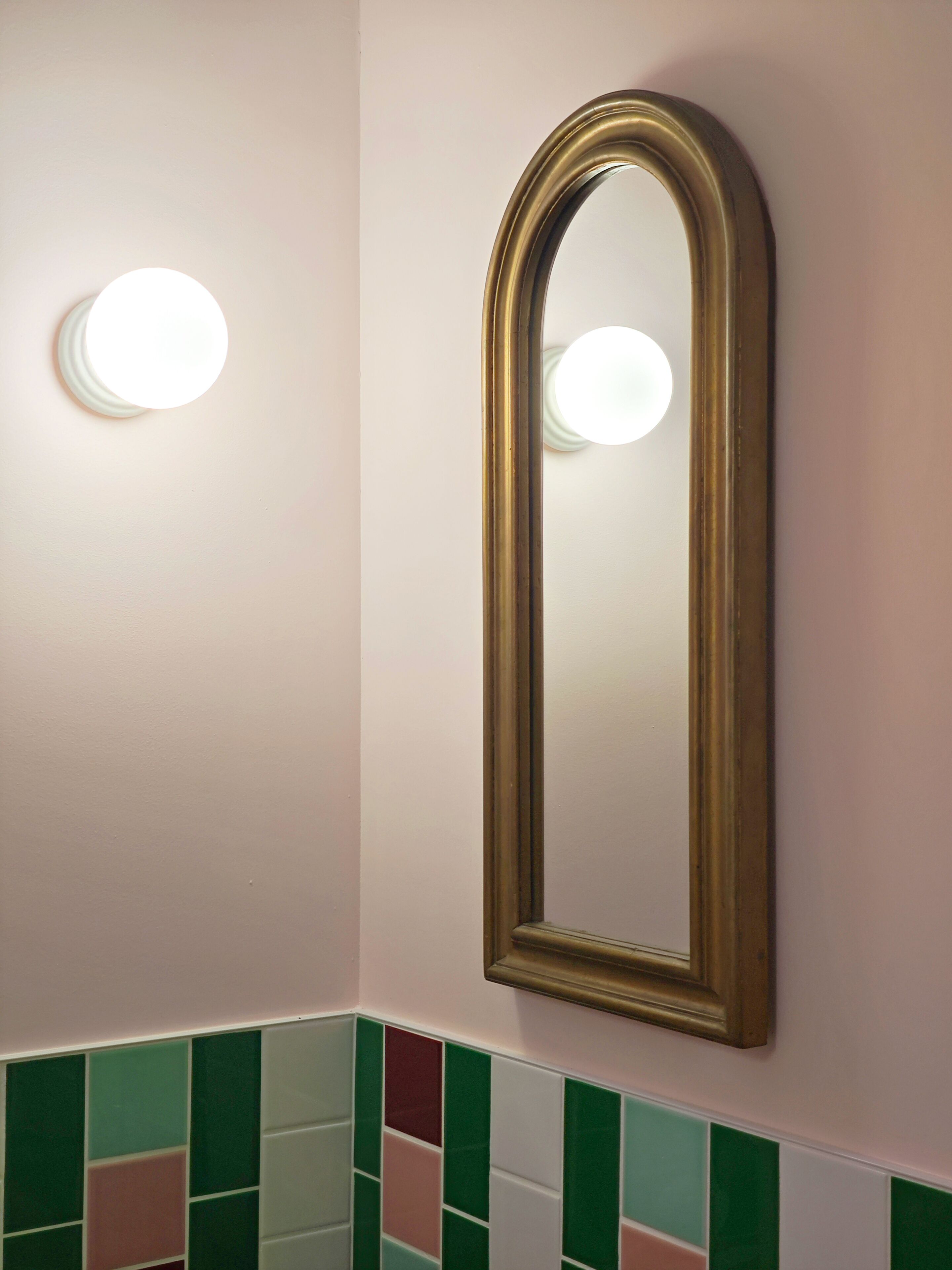 A bathroom with a wall-mounted mirror and a light fixture above it.