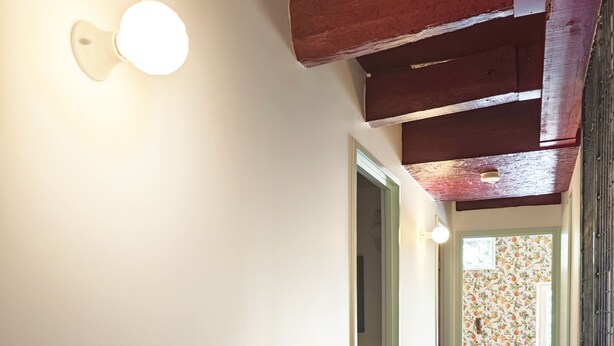 Un couloir doté d’un plancher en bois, d’un luminaire fixé au mur et d’une porte donnant sur une autre pièce.