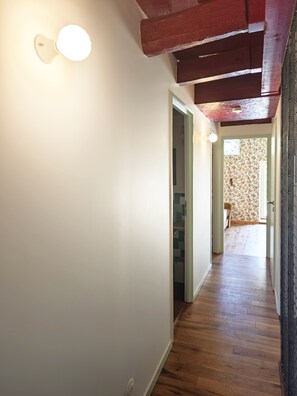 Un pasillo con piso de madera, una lámpara en la pared y una puerta que da a otra habitación.