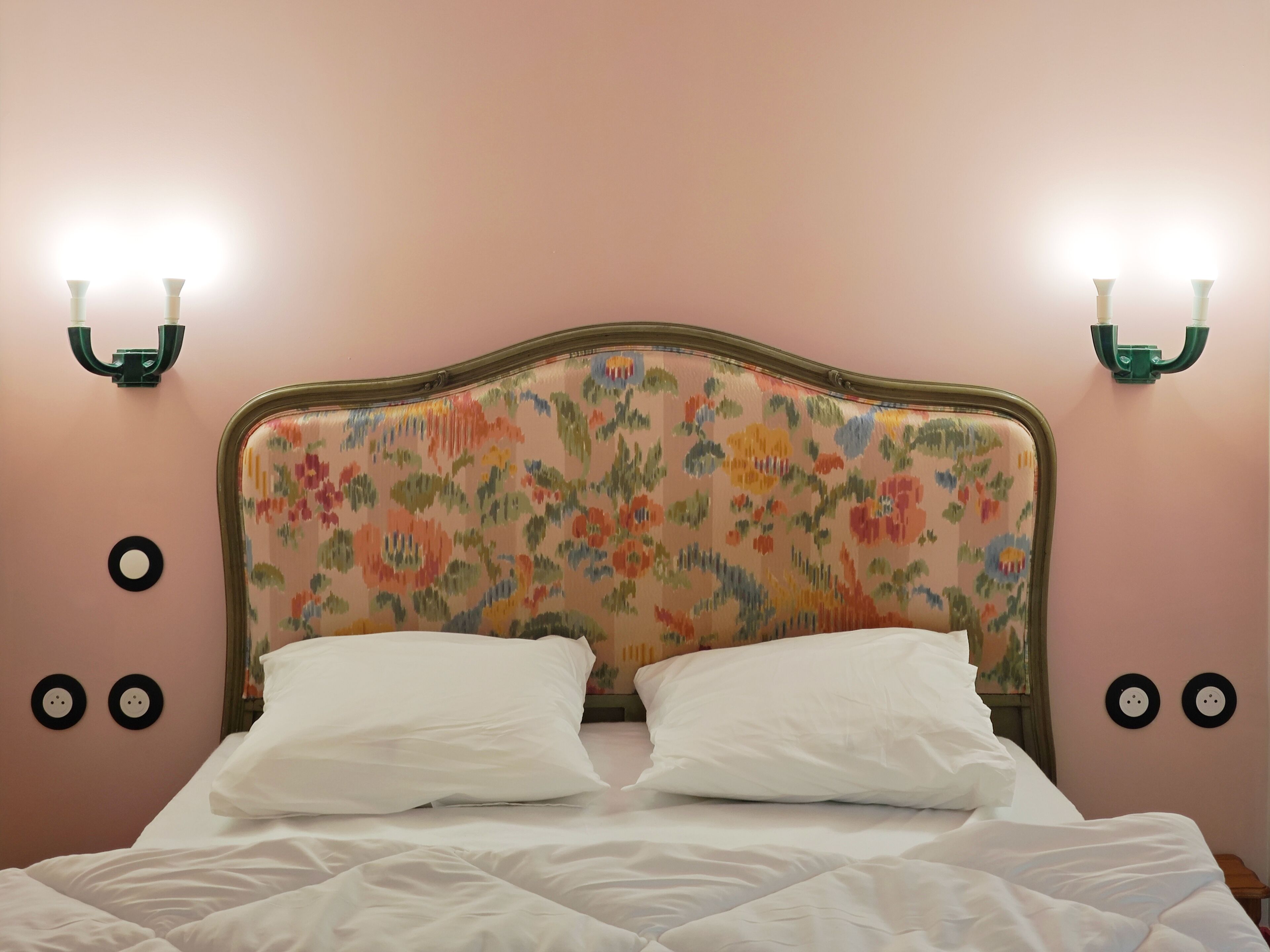 Un lit avec une tête de lit à motifs floraux, deux appliques murales et des décorations murales rondes.
