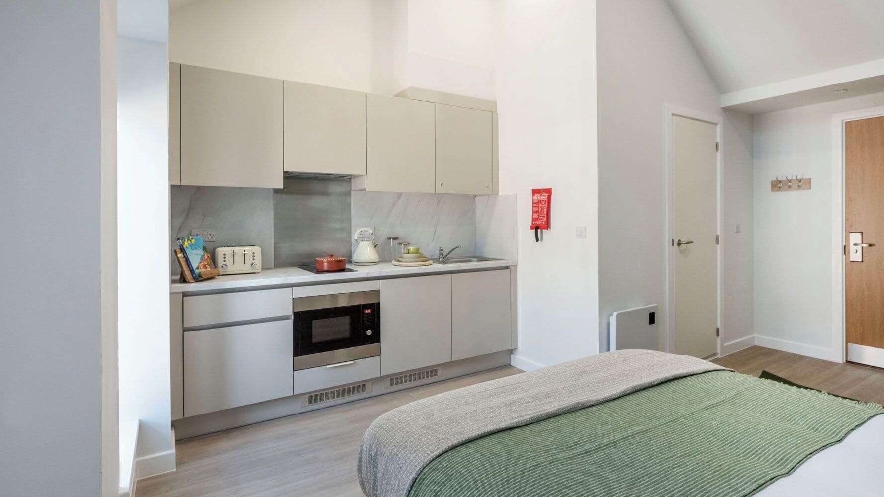 A compact kitchen with a microwave, oven, and a small countertop with a kettle and a book.