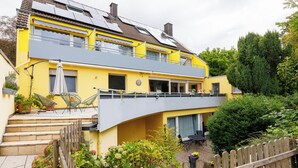 Ein zweistöckiges Gebäude mit Balkon, Außenbereich zum Sitzen und einem Garten.