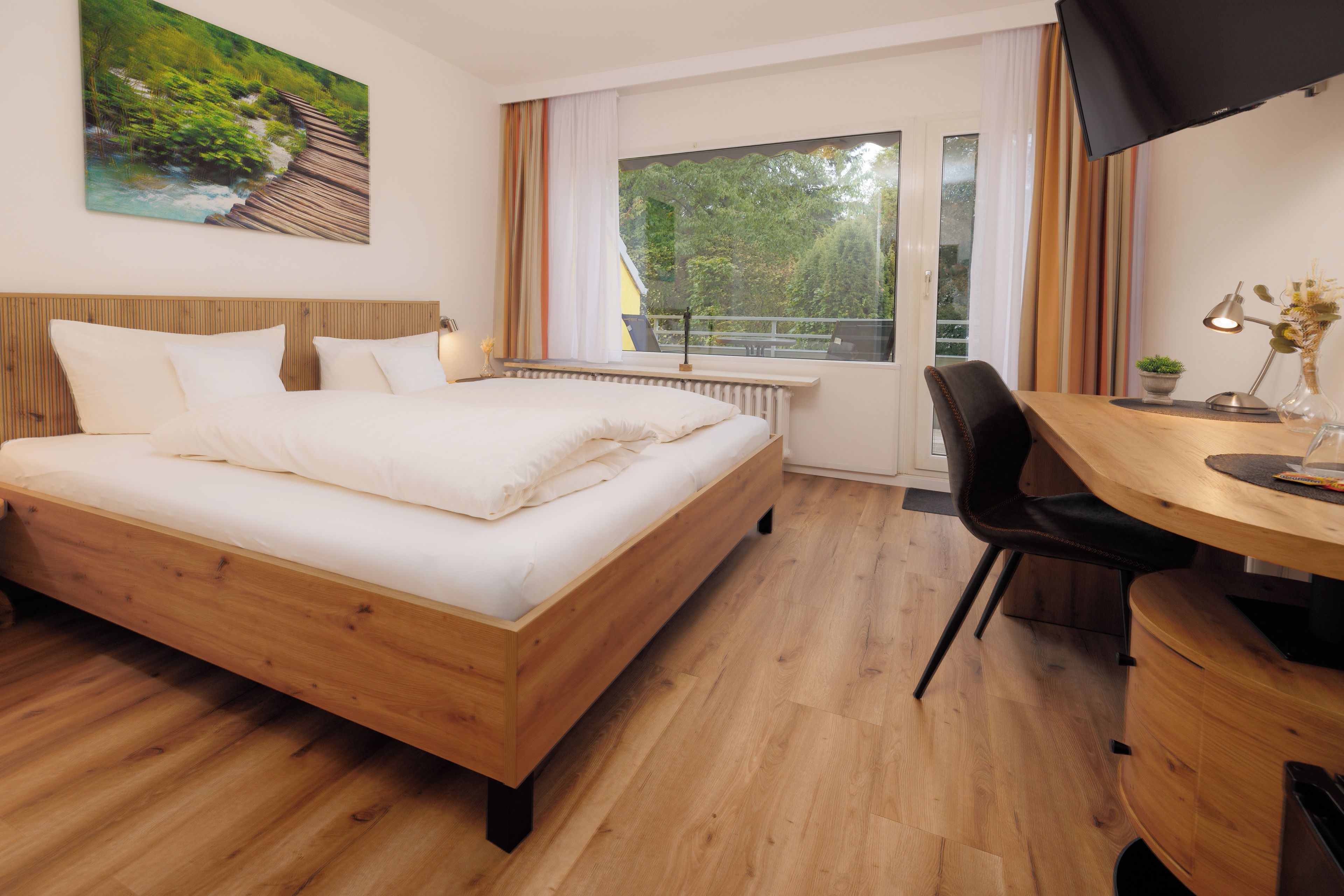 A hotel room with a wooden bed, a desk with a chair, a TV, and a window with curtains.