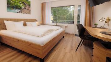 A hotel room with a wooden bed, a desk with a chair, a TV, and a window with curtains.