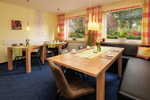 Een eetgedeelte met houten tafels en stoelen, een buffetopstelling en uitzicht op groen buiten.