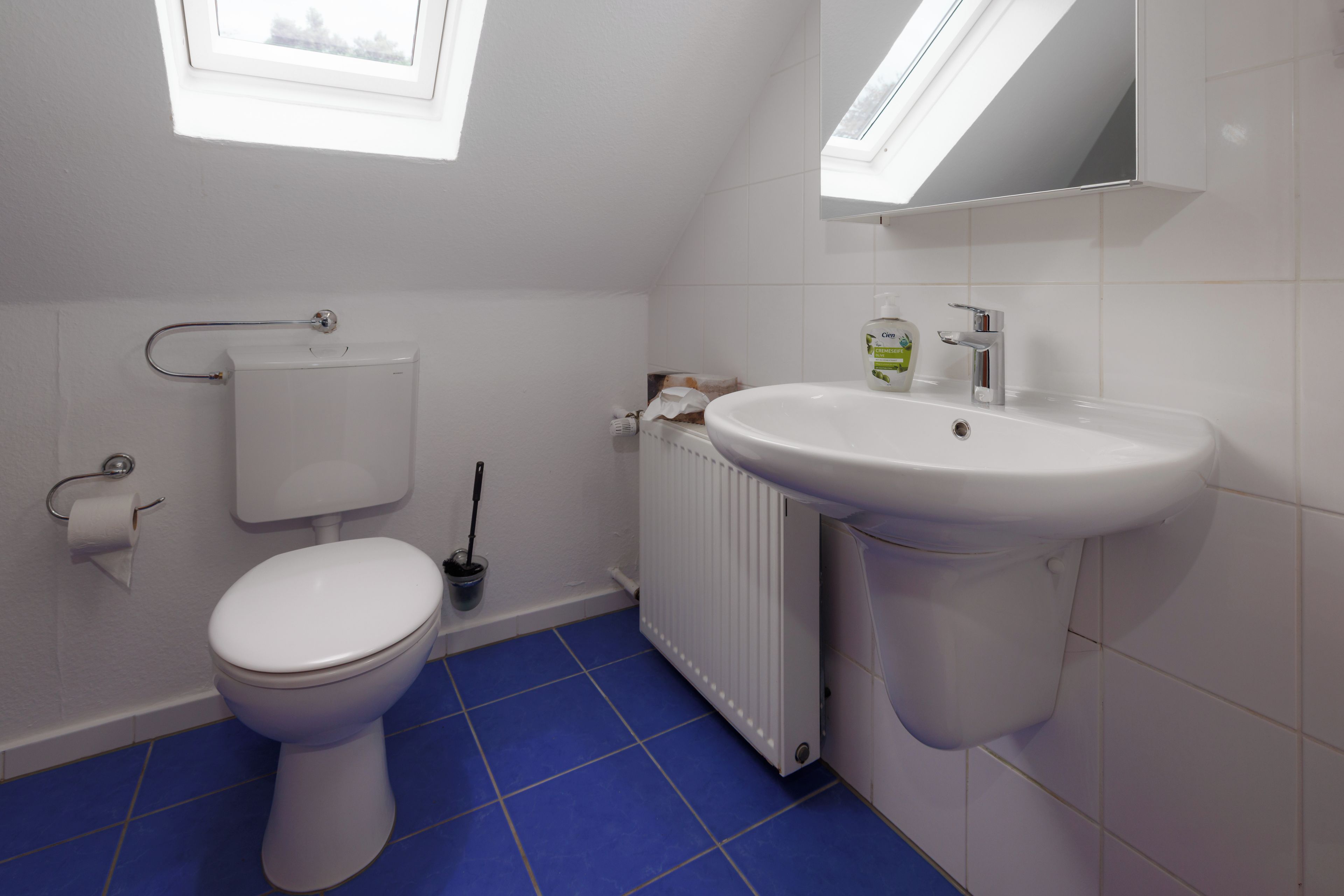 A bathroom with a toilet, a sink, a radiator, and a window.