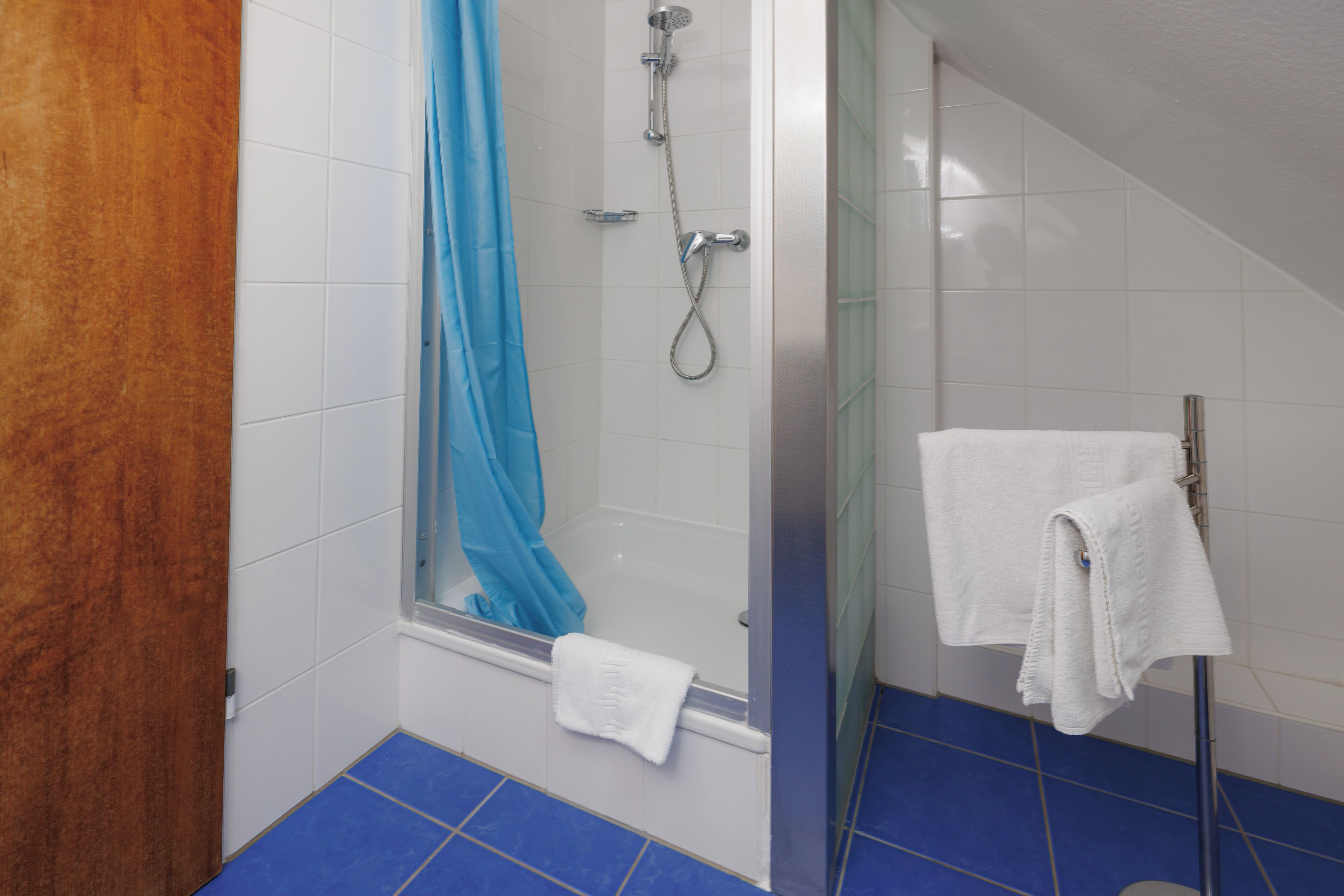 A bathroom with a glass shower enclosure, a blue shower curtain, and a white towel on a rack.